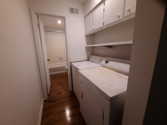 clothes washing area with washing machine and dryer, cabinets, and dark hardwood / wood-style floors