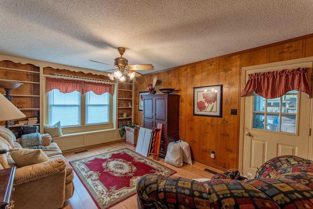 living room featuring ceiling fan, a textured ceiling, wood walls, and light wood-type flooring