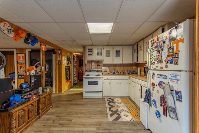 kitchen with a drop ceiling, wood walls, white appliances, white cabinetry, and light wood-type flooring