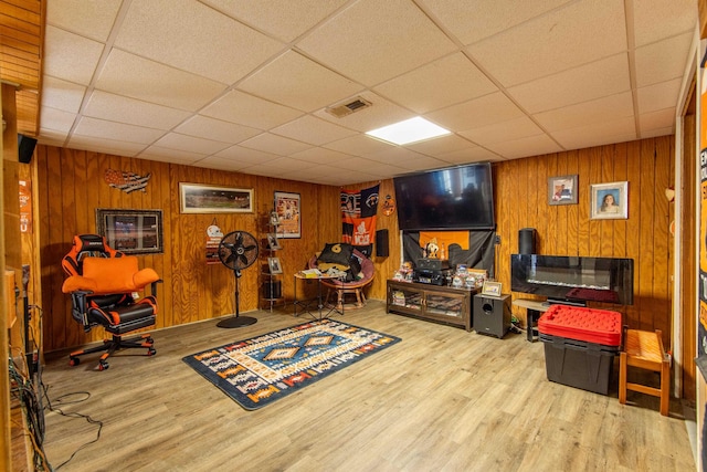 interior space with a paneled ceiling, light wood-type flooring, and wood walls