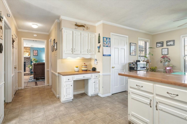 kitchen featuring a textured ceiling, ornamental molding, butcher block counters, and white cabinets