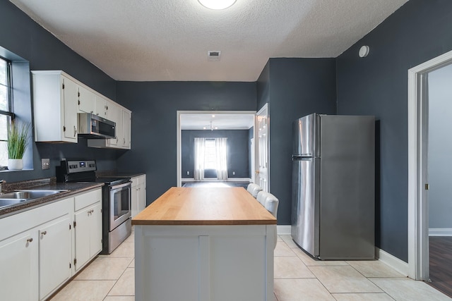 kitchen featuring a center island, light tile patterned flooring, a textured ceiling, stainless steel appliances, and white cabinets