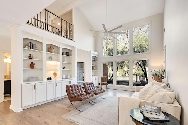 living room with ceiling fan, a high ceiling, and light wood-type flooring