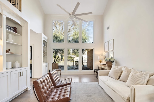 living room with ceiling fan, built in shelves, dark hardwood / wood-style flooring, and a towering ceiling