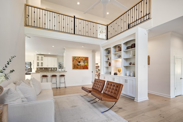 living room with ceiling fan, a high ceiling, and light hardwood / wood-style floors