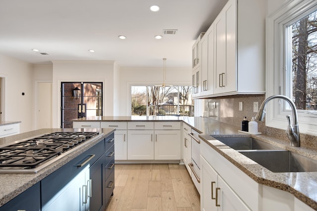 kitchen featuring stainless steel gas cooktop, light stone countertops, sink, and white cabinetry