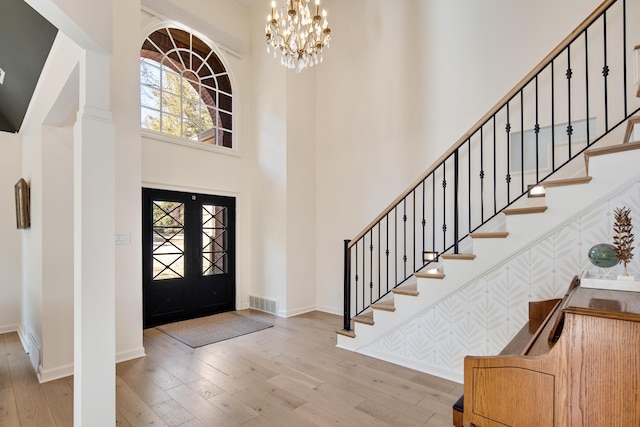 entryway with a towering ceiling, a notable chandelier, french doors, and light wood-type flooring