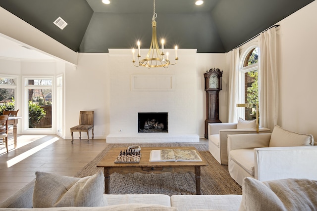 living room featuring high vaulted ceiling, a brick fireplace, wood-type flooring, and a notable chandelier