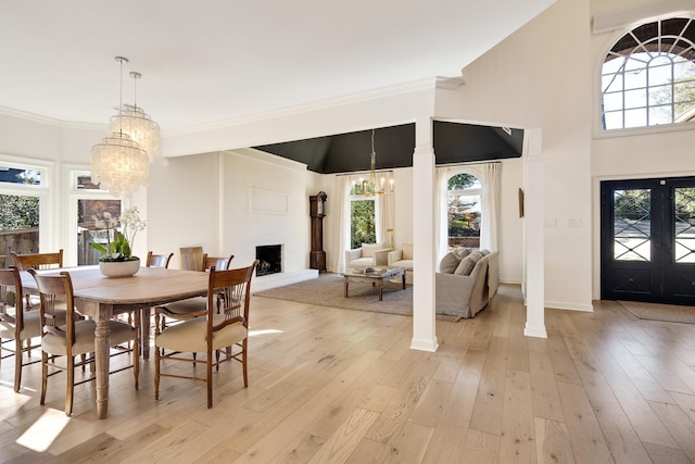 dining space with light wood-type flooring, ornate columns, a fireplace, and a notable chandelier