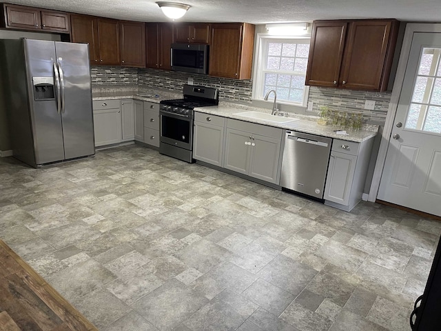 kitchen featuring light stone countertops, decorative backsplash, appliances with stainless steel finishes, and sink