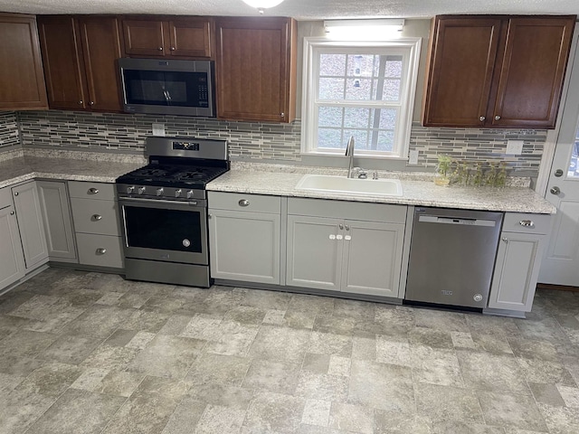 kitchen featuring sink, backsplash, appliances with stainless steel finishes, and gray cabinetry