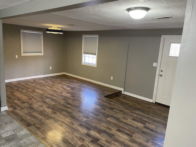 basement featuring a textured ceiling, dark wood-type flooring, and plenty of natural light