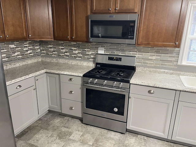 kitchen with tasteful backsplash, light stone countertops, appliances with stainless steel finishes, and sink