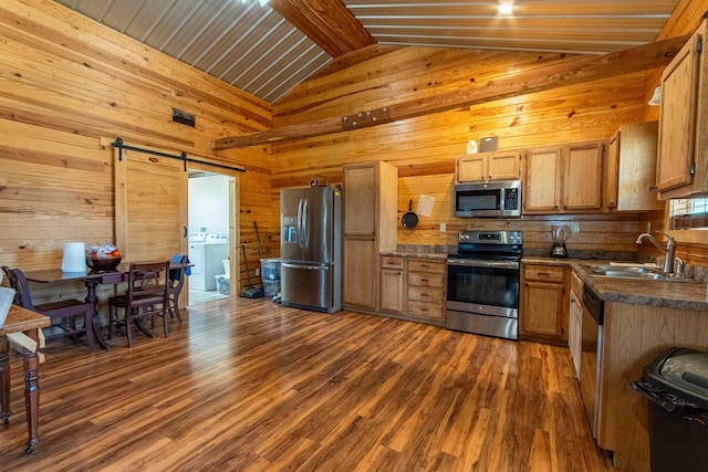 kitchen with a barn door, vaulted ceiling with beams, sink, dark wood-type flooring, and stainless steel appliances