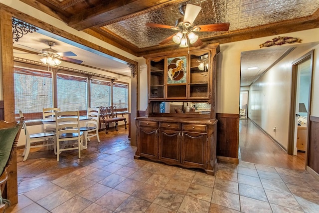 interior space with ceiling fan, beamed ceiling, ornamental molding, and dark brown cabinetry