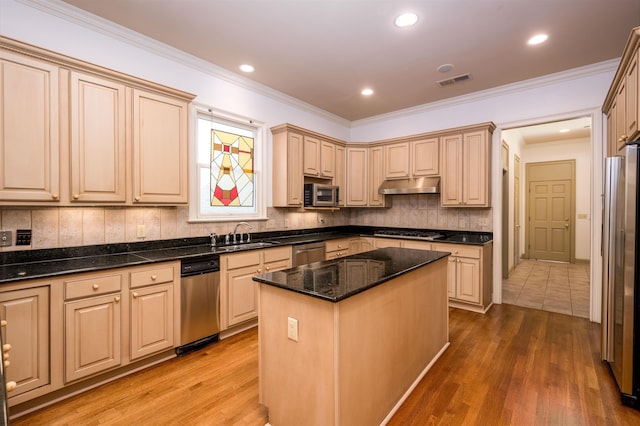 kitchen featuring light brown cabinetry, a center island, stainless steel appliances, and dark stone counters