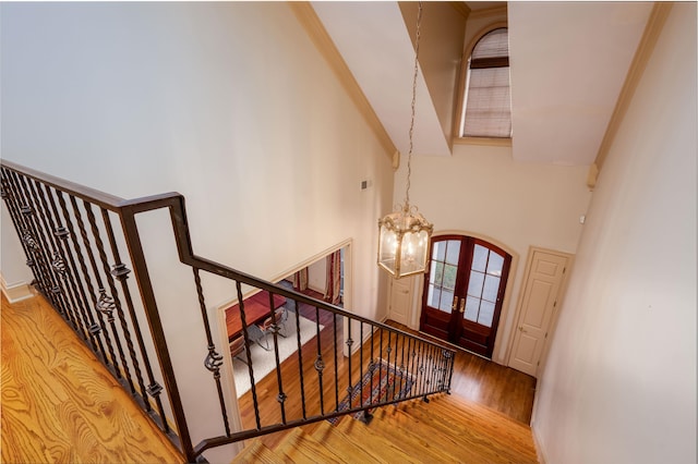 stairway with hardwood / wood-style flooring, a chandelier, a towering ceiling, and french doors