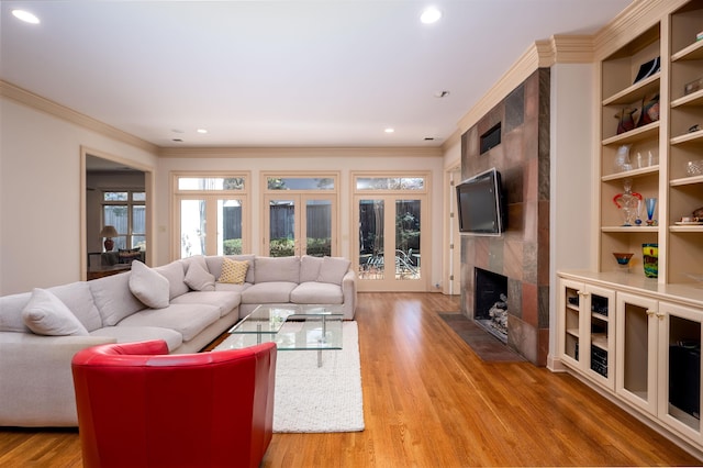 living room with light wood-type flooring, built in features, french doors, a high end fireplace, and crown molding