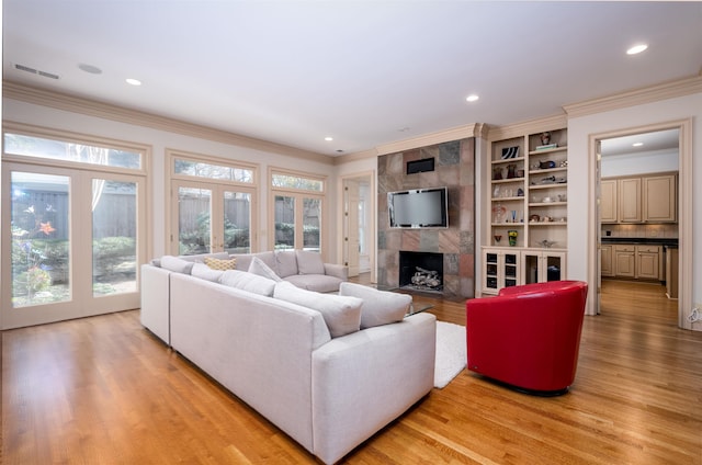 living room featuring french doors, a fireplace, built in features, light wood-type flooring, and crown molding