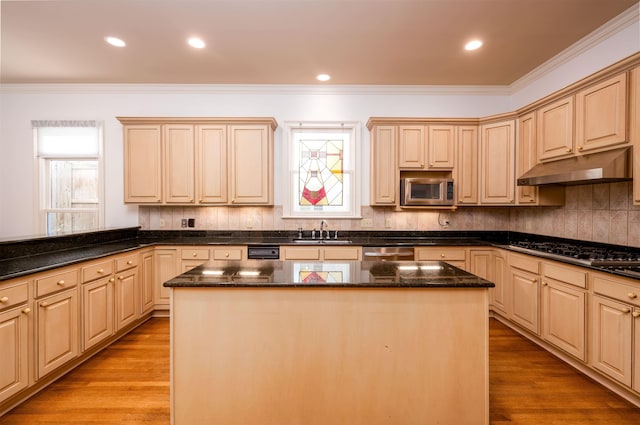 kitchen with appliances with stainless steel finishes, a center island, dark stone counters, light brown cabinetry, and sink