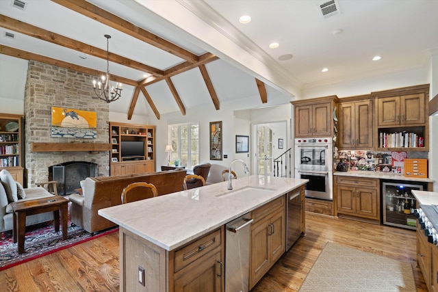 kitchen with beverage cooler, a stone fireplace, sink, hanging light fixtures, and a center island with sink