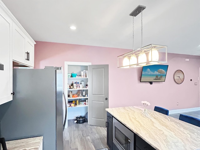 kitchen featuring light hardwood / wood-style floors, white cabinetry, hanging light fixtures, stainless steel appliances, and a breakfast bar area