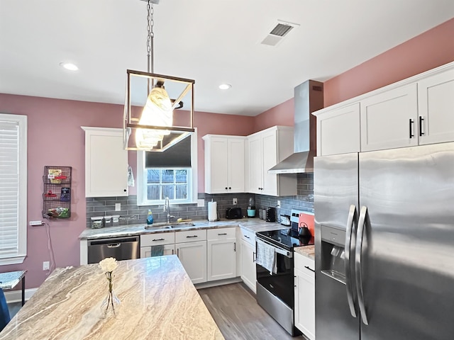 kitchen featuring white cabinets, sink, pendant lighting, stainless steel appliances, and wall chimney exhaust hood