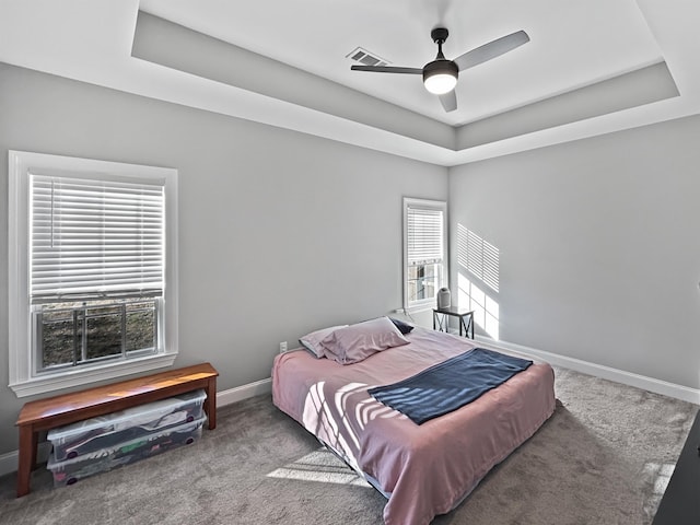 carpeted bedroom with ceiling fan and a raised ceiling