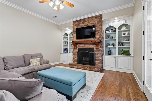 living room featuring built in shelves, a fireplace, dark hardwood / wood-style floors, ornamental molding, and ceiling fan