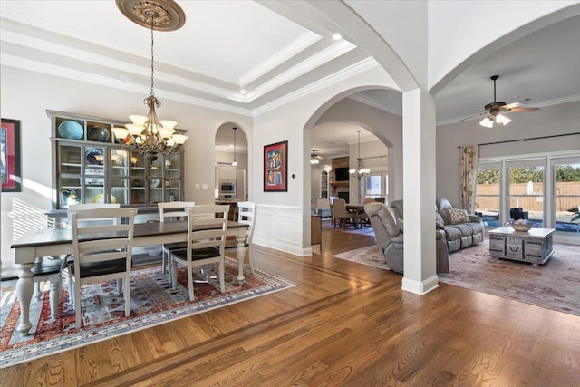 dining space with a raised ceiling, crown molding, ceiling fan with notable chandelier, and wood-type flooring