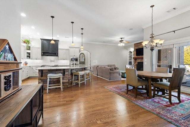 dining space featuring crown molding, wood-type flooring, a stone fireplace, and ceiling fan with notable chandelier