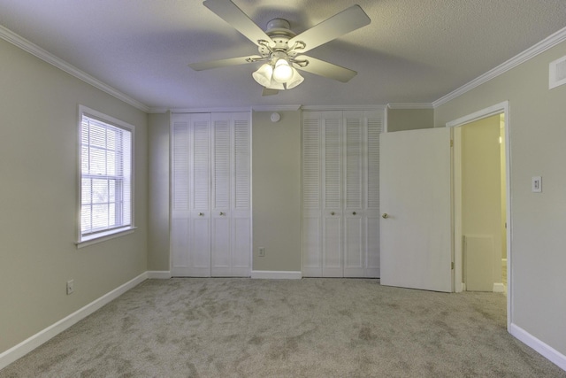 unfurnished bedroom featuring light carpet, multiple closets, crown molding, and ceiling fan