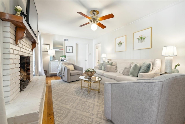 living room with ceiling fan, light wood-type flooring, a brick fireplace, and ornamental molding