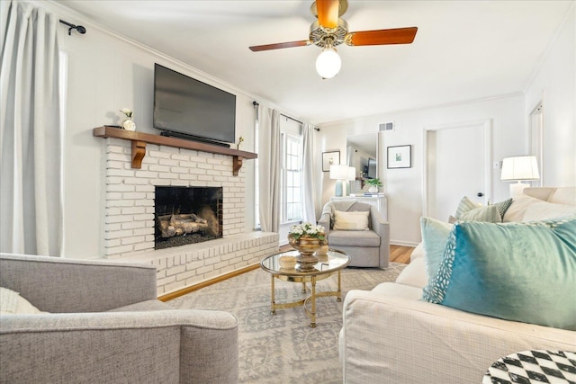 living room featuring a brick fireplace, crown molding, ceiling fan, and light wood-type flooring