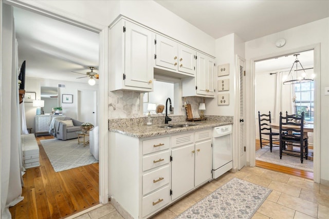 kitchen with tasteful backsplash, sink, white dishwasher, white cabinets, and ceiling fan with notable chandelier