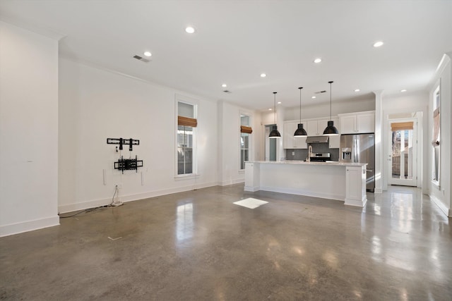 kitchen featuring decorative light fixtures, white cabinetry, stainless steel appliances, an island with sink, and concrete floors