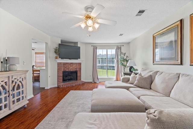 living room with a brick fireplace, a textured ceiling, dark hardwood / wood-style floors, and ceiling fan