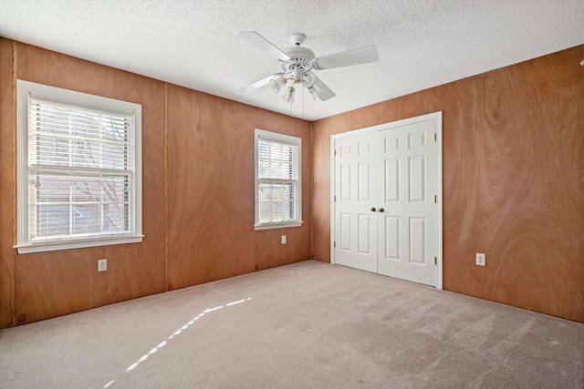 unfurnished bedroom featuring a textured ceiling, light carpet, a closet, wood walls, and ceiling fan