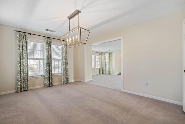 carpeted empty room featuring a textured ceiling and a notable chandelier