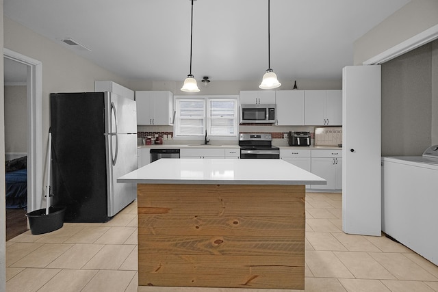 kitchen featuring appliances with stainless steel finishes, tasteful backsplash, hanging light fixtures, white cabinets, and washer / clothes dryer