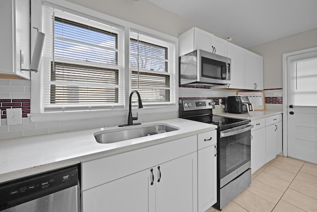 kitchen featuring backsplash, sink, light tile patterned flooring, white cabinetry, and appliances with stainless steel finishes