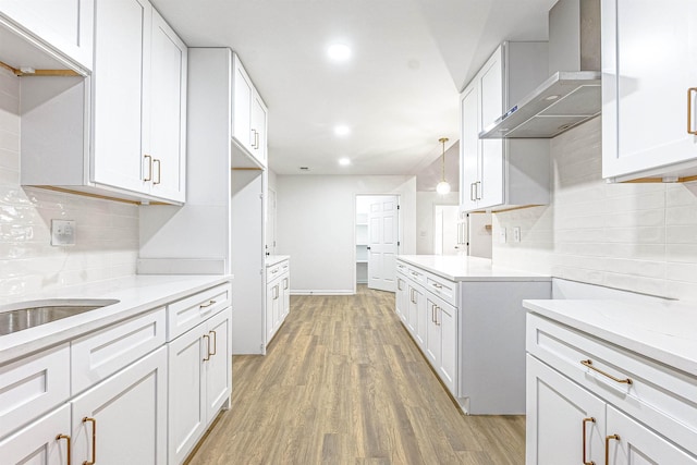 kitchen with hardwood / wood-style floors, backsplash, hanging light fixtures, wall chimney exhaust hood, and white cabinets