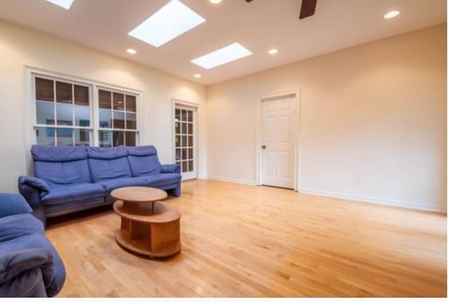 living room with light wood-type flooring, ceiling fan, and a skylight