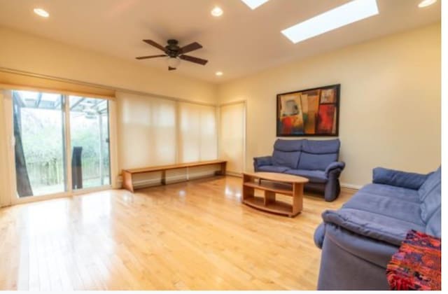 living room featuring ceiling fan, hardwood / wood-style flooring, and a skylight