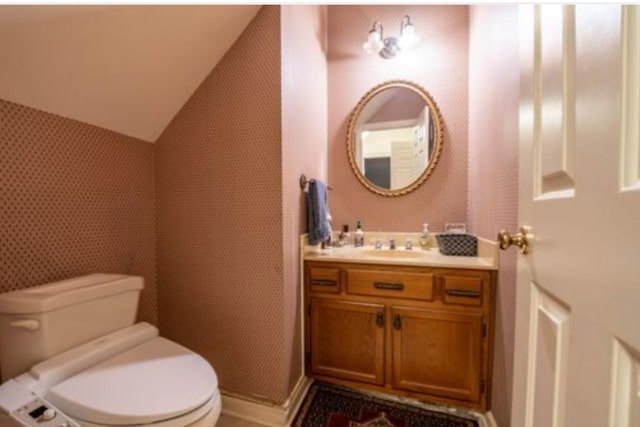 bathroom with toilet, vanity, and lofted ceiling