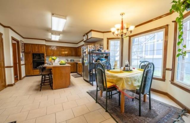 tiled dining room with plenty of natural light, an inviting chandelier, and ornamental molding