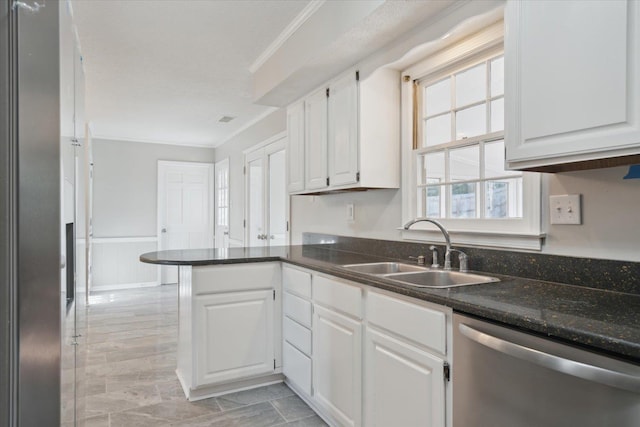 kitchen featuring stainless steel appliances, ornamental molding, white cabinets, a sink, and a peninsula