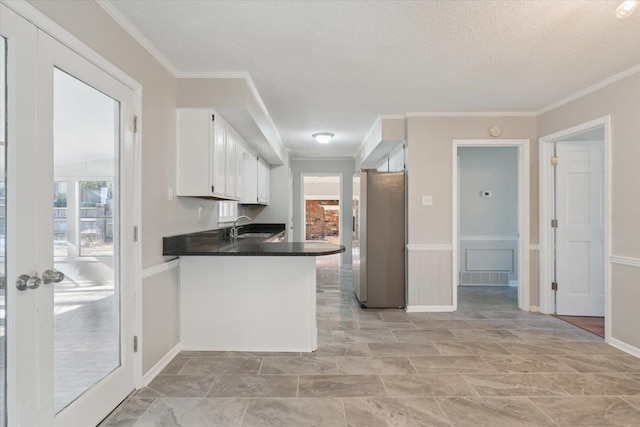 kitchen featuring dark countertops, freestanding refrigerator, white cabinets, a sink, and a peninsula