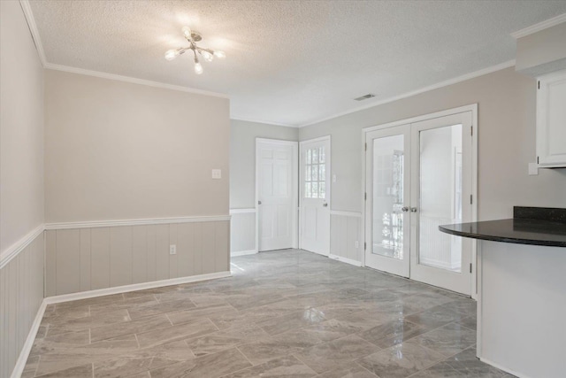 interior space with a textured ceiling, a wainscoted wall, visible vents, french doors, and ornamental molding