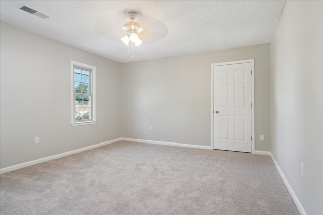 empty room featuring a ceiling fan, light colored carpet, visible vents, and baseboards